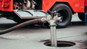 Heavy-duty industrial pumping equipment is connected to a street manhole via a large suction hose.